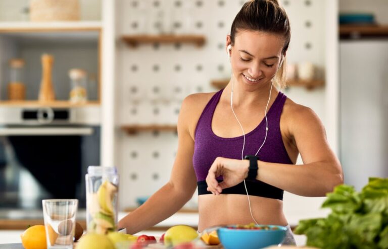 happy-athletic-woman-checking-time-her-wristwatch-while-preparing-fruit-smoothie-kitchen-min-1170x752